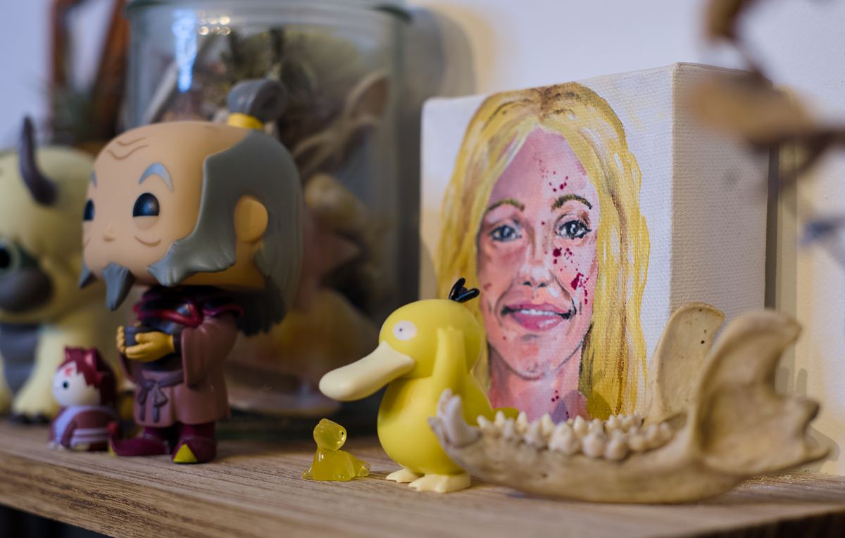 A small painted portrait beside Funko Pop figurines and a Psyduck on a wooden shelf.