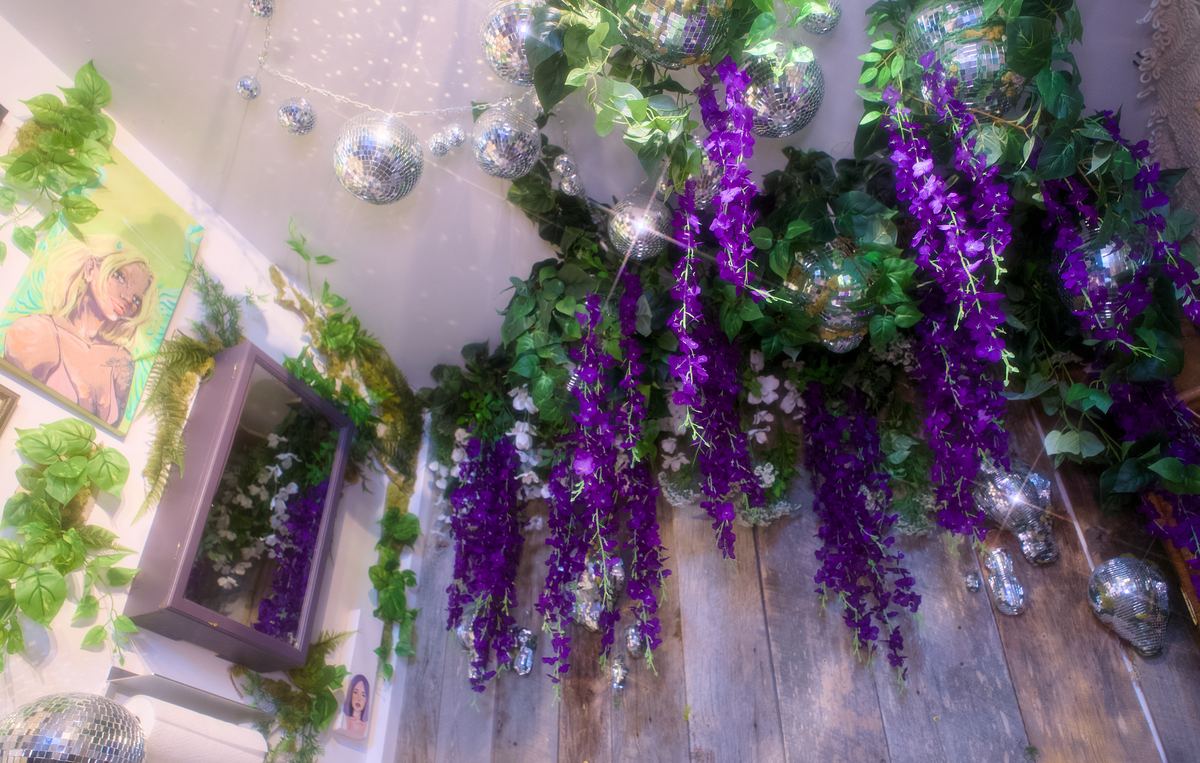 Hanging purple wisteria, disco balls, and a painted portrait near the studio's entrance.
