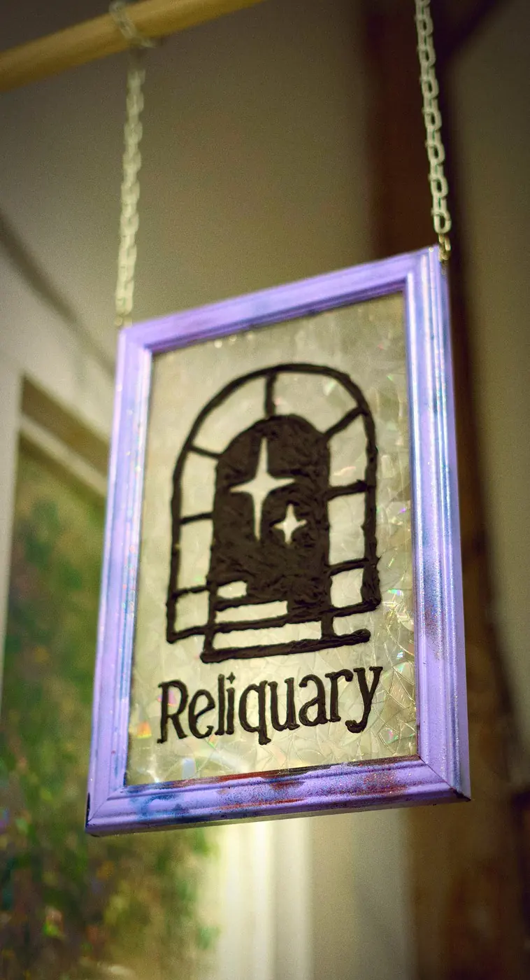 A hanging sign in a lilac frame: Reliquary's arched window with two stars, over the hall outside the studio.